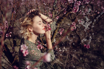 fashion outdoor photo of gorgeous young woman in elegant dress posing in garden with blossom peach trees