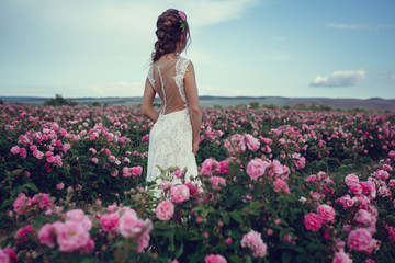 Beautiful woman in a floral park, garden roses. Makeup, hair, a wreath of roses.
