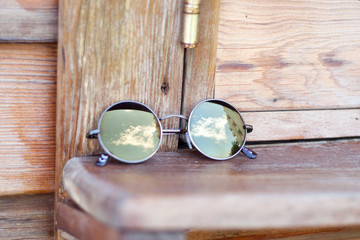 Fototapeta na wymiar Sunglasses at the wooden windowsill., with beautyfill sky and clouds reflected