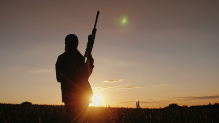 Silhouette of a woman with a rifle. A sieve in the field at sunset. Sports shooting concept. Back...