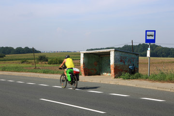 Rowerzysta z flagą na tle starego przystanku autobusowego. - obrazy, fototapety, plakaty