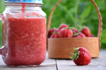 Healthy strawberry smoothie in a mason a jar mug over a rustic wood background against of green foliage in the garden