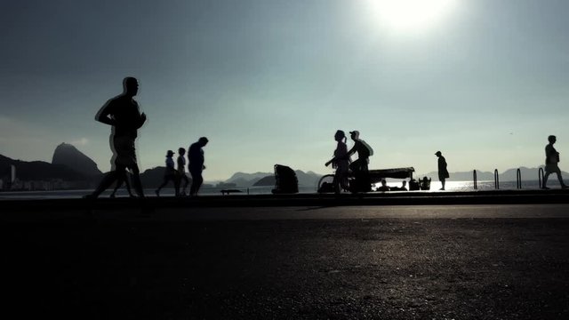 Silhouettes walking, running, and cycling on the beachfront road at Copacabana Beach, Rio de Janeiro, Brazil