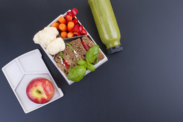 Delicious lunch in a container for school and office. Sandwich, vegetables, apple and green juice for a healthy lunch. Top view on a black background. Copy space.