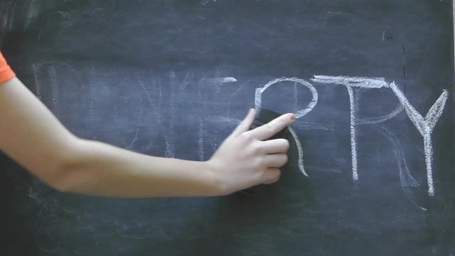 Erasing the word poverty written in white chalk on a black chalkboard
