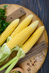Young corn cobs with leaves, spices, herbs, sea salt on a wooden tray. Top view.