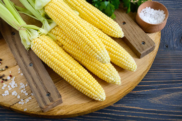 Young corn cobs with leaves, spices, herbs, sea salt on a wooden tray. Top view.