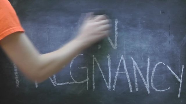 Erasing the word teen pregnancy written in white chalk on a black chalkboard