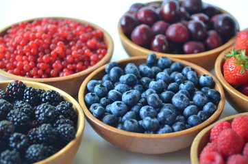 Detail of fresh summer fruit and berries in wooden bowls. Strawberries, raspberries, cherries, blackberries, blueberries and red currants top view.
