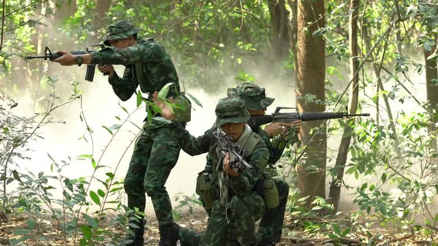 Soldier holding gun weapon and waring armor uniform with smoke camouflage in forest. The military is responsible for maintaining the territory.
