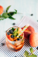 The glass of peach ice tea on wooden table. Cuba Libre or long island iced tea cocktail, cold drink or lemonade with fruits and mint, bilberry, blueberry