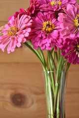 a bouquet of pink zinnia flowers in a vase, on wood
