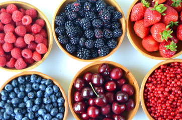 Detail of fresh summer fruit and berries in wooden bowls. Strawberries, raspberries, cherries, blackberries, blueberries and red currants top view.
