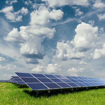 Solar panel on blue sky background. Green grass and cloudy sky. Alternative energy concept