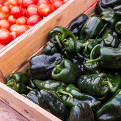 Wooden bins of dark green pasilla peppers and red tomatoes at a farmer's market.