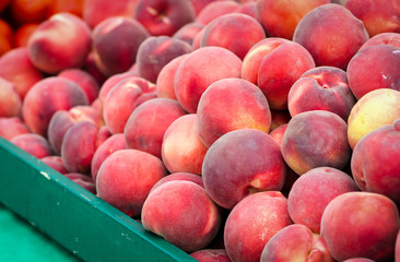A large pile of fresh peaches in a green wood bin at the Clement Street Farmer's Market in San Francisco.
