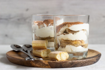 Traditional Italian dessert tiramisu in glass on light grey background. Coffee flavored Italian dessert made of ladyfingers and mascarpone. 