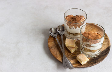 Traditional Italian dessert tiramisu in glass on light grey background. Coffee flavored Italian dessert made of ladyfingers and mascarpone. 