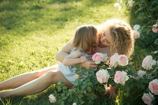 Mom kissing daughter on green grass on sunny summer day
