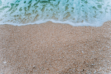 Rolling soft foam wave of blue turquoise sea water on pebble beach. Background. Top view
