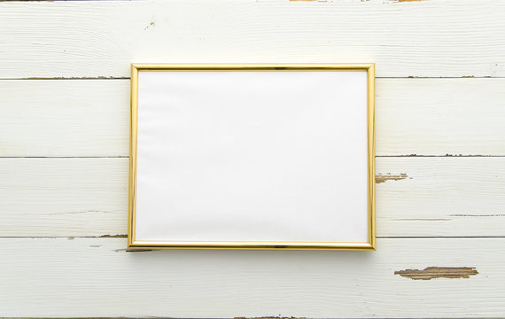 Golden photo frame for painting or picture on white wooden background. Flat lay, top view. Horisontal mockup