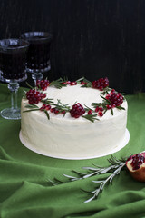 Chocolate cake with berry cream, white cheese cream, pomegranate berries and rosemary branches. Two glasses of red wine. Idea for a birthday cake or for a wedding cake.