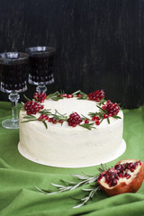 Naklejka premium Chocolate cake with berry cream, white cheese cream, pomegranate berries and rosemary branches. Two glasses of red wine. Idea for a birthday cake or for a wedding cake.