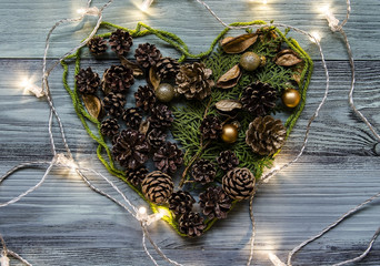 Heart made out from pine cones and other Christmas decorations. Wooden background with lights