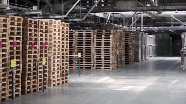 Warehouse with racks and shelves, filled with cardboard boxes, wrapped in foil on wooden pallets. Clip. Large and light warehouse, cargo storage in wooden boxes. Wooden pallets and cardboard boxes