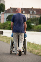 Fototapeta na wymiar portrait on back view of man pushing a wheelchair with invalid person in outdoor