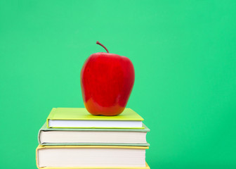 Close up on Hard bound books with various colored covers stacked with red apple on top, dark green background similar to old fashioned chalk board. Back to school concept.
