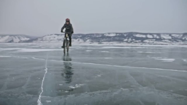 View of tire. Shooting 180fps. Man is riding bicycle on the ice. The cyclist cuts in front of the camera. Pieces of ice fly in us. Ice of the frozen Lake Baikal. The tires on the bicycle are covered