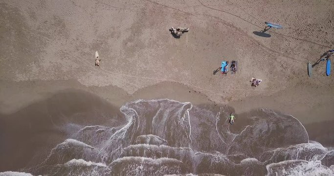 Aerial top view waves break on sand beach at sunset. Sea waves on the beautiful beach aerial view drone 4k shot. Bird's eye view of ocean waves and sporty surfers with surfing boards from above.