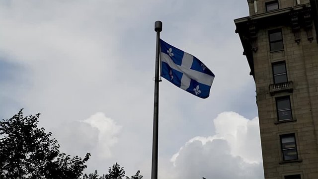 Quebec province flag blowing in the wind in Montreal. Fleur de lis flag flapping in the wind with a cloudy sky. French flag symbol flying in the wind. 