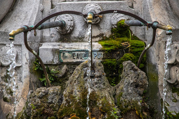 Closeup of an ancient stone French drinking fountain with moss growing on it