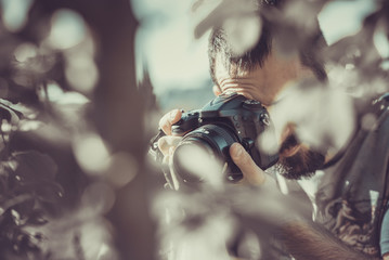 Young man using his dslr camera, photographing leaves and nature in spring