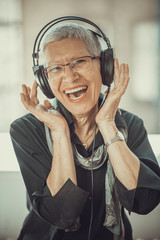 Senior old woman listening to her favourite music through big headphones, enjoying the rich sound