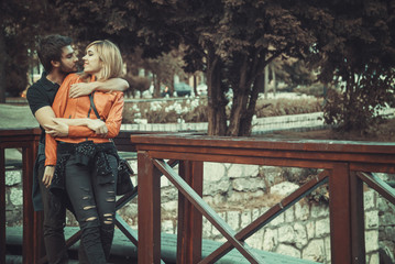 Happy young couple in a hug, kissing each other, standing on a small bridge in late autumn