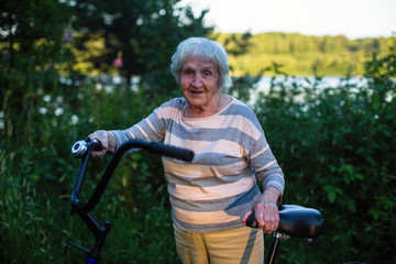 An elderly woman standing with a Bicycle.