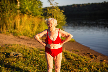 An elderly woman in a swimsuit is on the river bank.