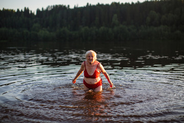 Elderly woman bathes and splashing in the river at sunset.