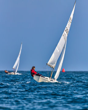 Competitors out on the blue Mediterranean Sea racing individual Finn Sailboats with the red turn marker in the distance