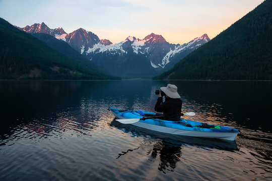 Adventure photographer on a kayak in the water surrounded by the Beautiful Canadian Mountain Landscape. Taken in Jones Lake, near Hope, East of Vancouver, BC, Canada.