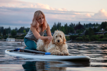 Girl with a dog on a paddle board during a vibrant summer sunset. Taken in Deep Cove, North Vancouver, BC, Canada.