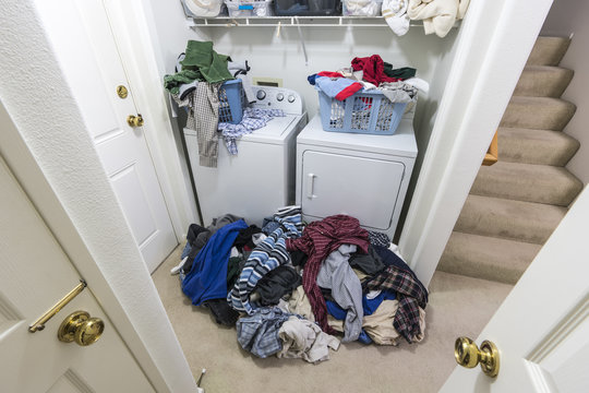 Cluttered Messy Laundry Room With Piles Of Clothes Needing To Be Washed.  