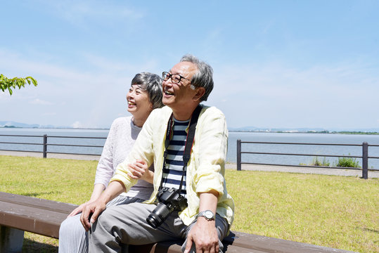 公園のベンチにで笑顔を浮かべるシニア夫婦