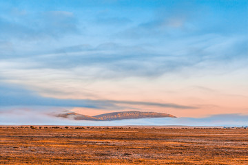 Barren land and rugged cliffs with low morning clouds at sunrise. Flinders Ranges, South Australia