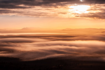 Fototapeta na wymiar Mountain peaks protruding through low clouds at beautiful sunrise