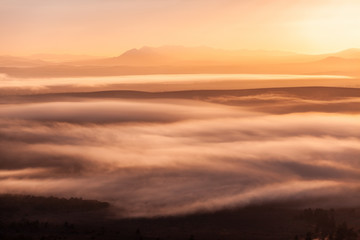 Mountain peaks protruding through low clouds at scenic glowing sunset