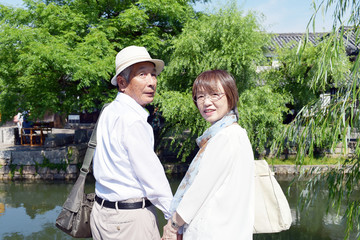旅先の川辺で、笑顔で振り返るシニア夫婦